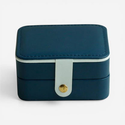 Boîte à bijoux bleu marine, fermée avec bouton doré et design compact élégant.