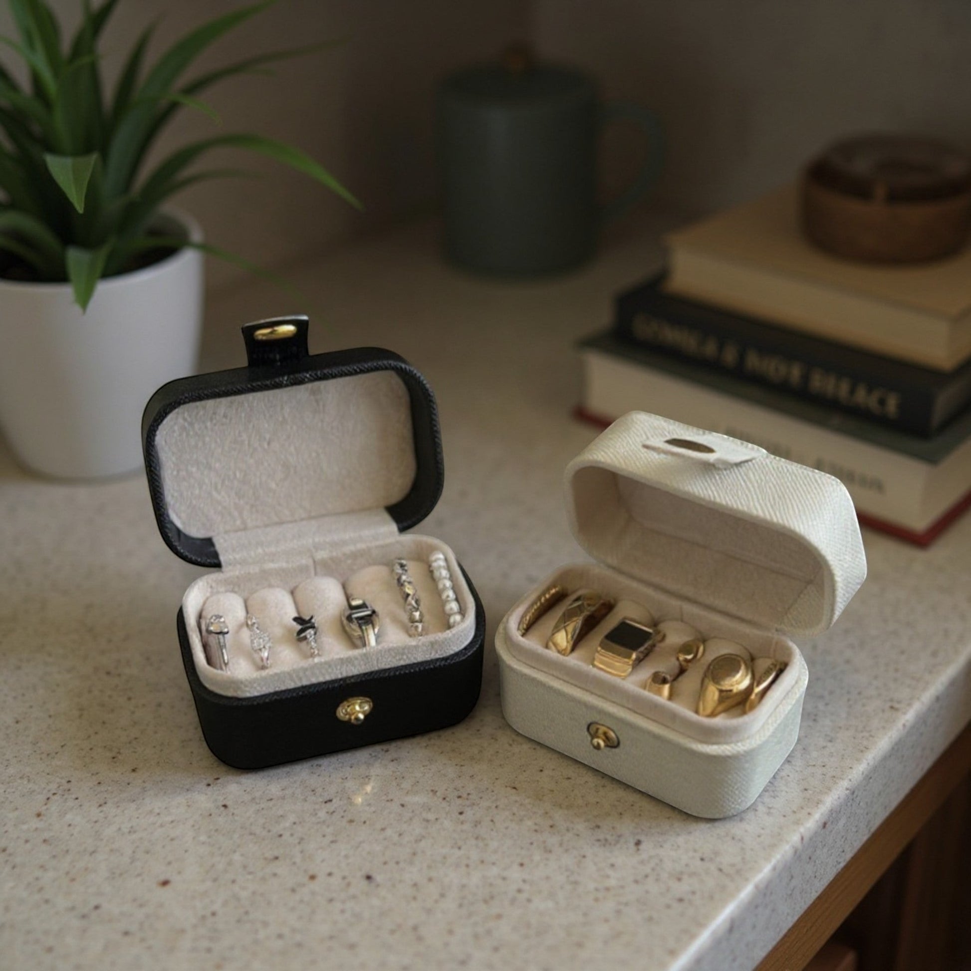 Boîtes à bijoux compactes noir et blanc, ouvertes sur une table avec bagues et accessoires dans un intérieur élégant.