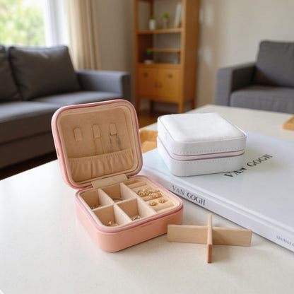Boîte à bijoux rose ouverte avec compartiments, posée sur une table dans un salon moderne.