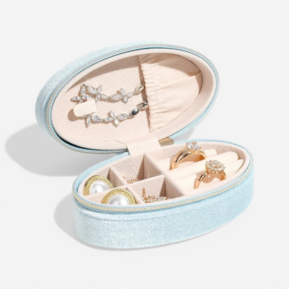 Boîte à bijoux ovale en velours bleu clair, ouverte avec des compartiments pour bagues et colliers.
