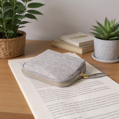 Sac organisateur de bijoux en velours gris avec fermeture zippée et pompon, posé sur une table.