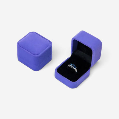 Boîte à bijoux carrée SecretGleam en velours violet avec une bague à l'intérieur sur fond blanc