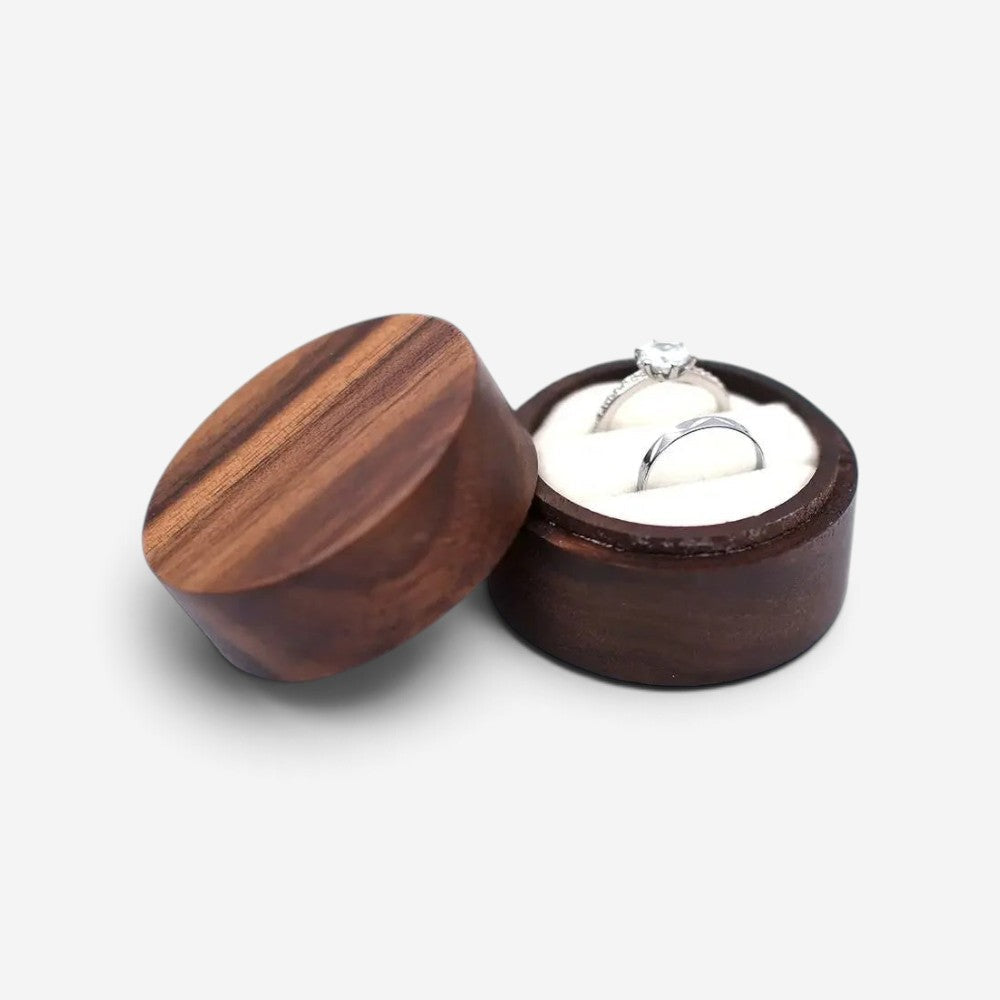 Écrin à bague rond en bois SecretGleam avec intérieur blanc et deux bagues en argent, couvercle en bois posé à côté