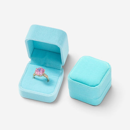 Mini boîte à bijoux SecretGleam en velours bleu ciel contenant une bague avec une pierre rose