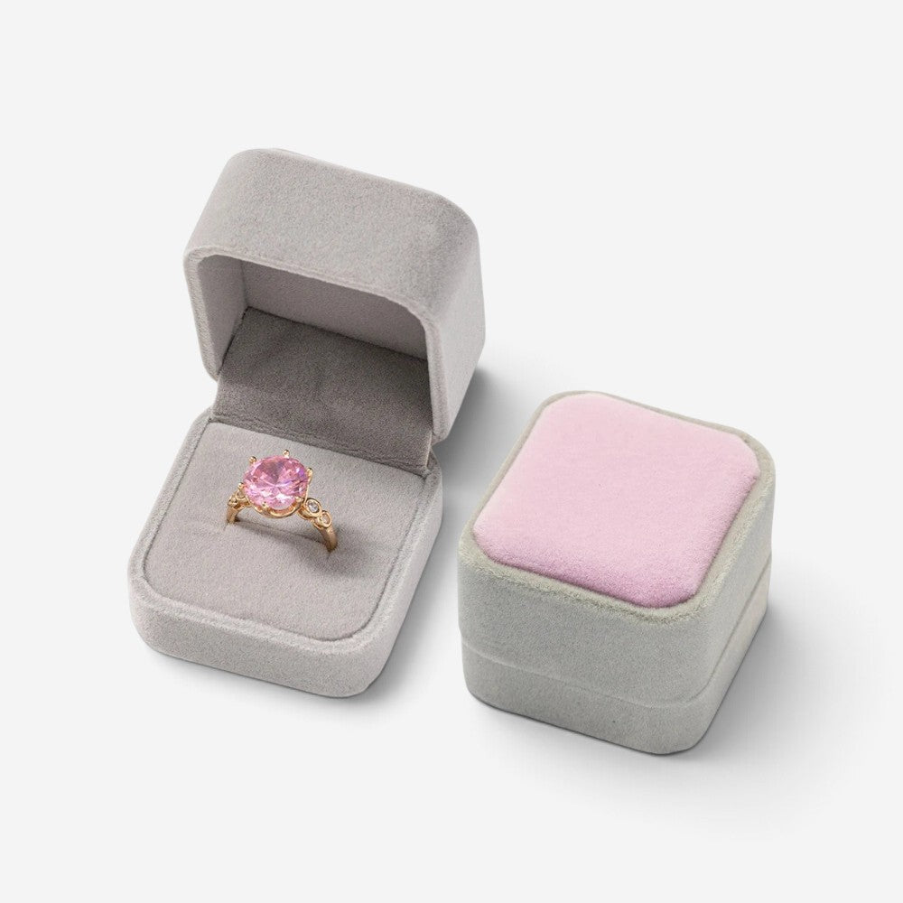 Mini boîte à bijoux SecretGleam en velours gris avec couvercle rose, contenant une bague dorée à pierre rose